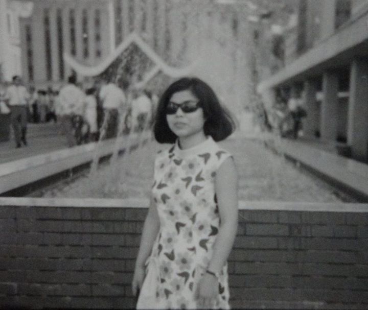 Black and white photo of my mom, wearing shades, standing in front of fountain